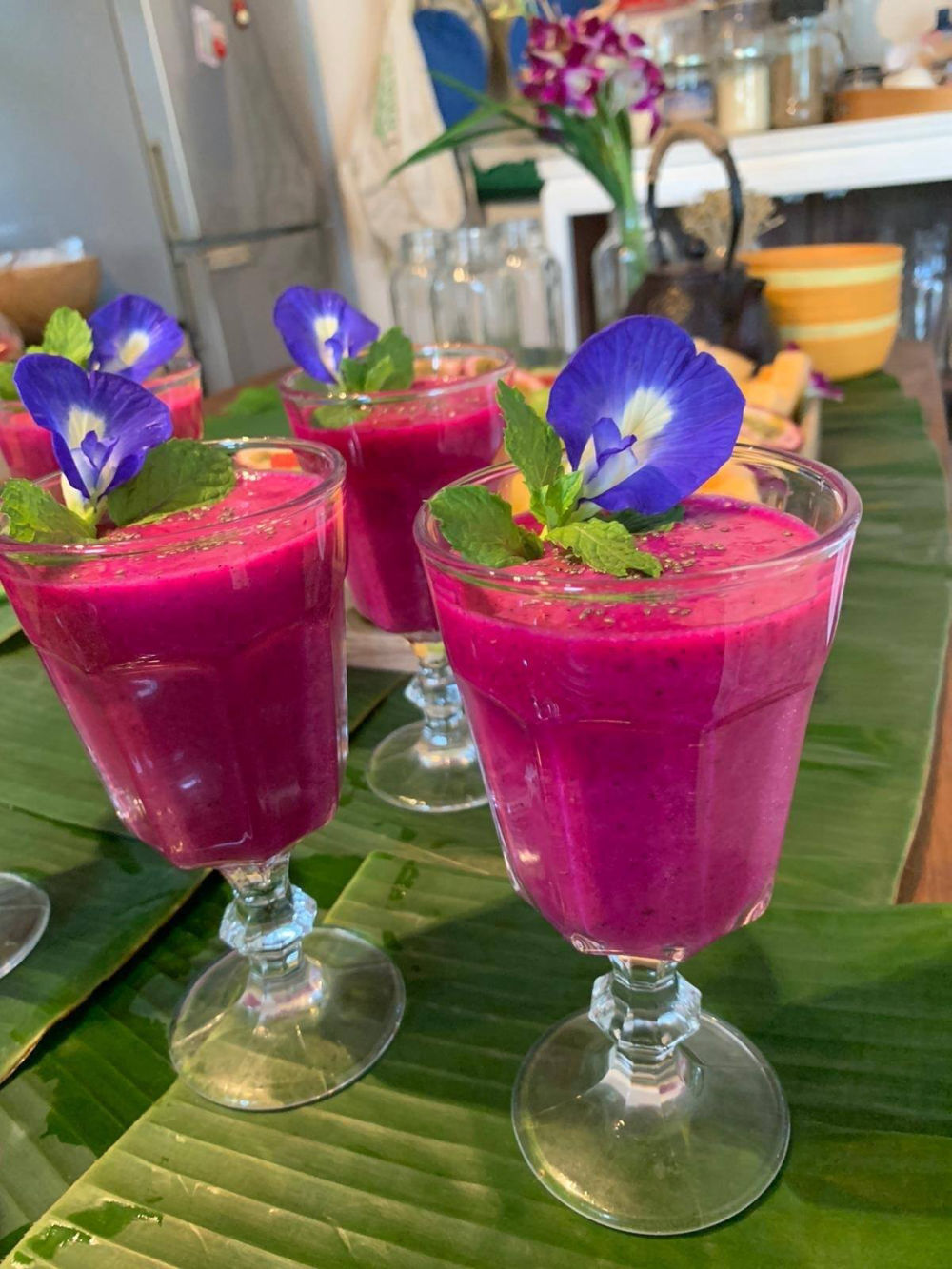 Magenta dragon-fruit refreshment cups garnished with butterfly-pea flowers on a banana leaf