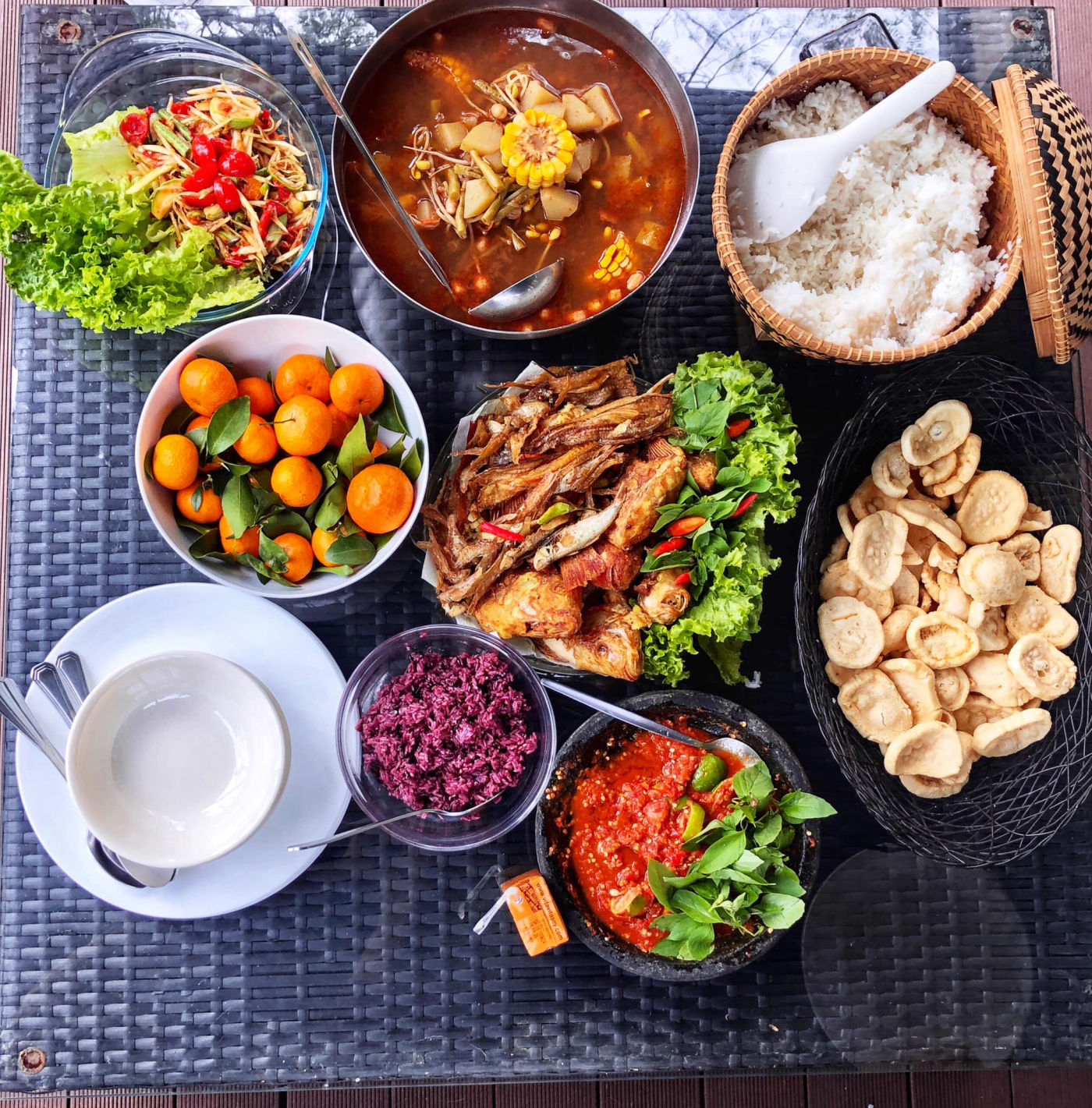 Stone mortar cobek filled with fresh sambal at the centre of an Indonesian feast spread