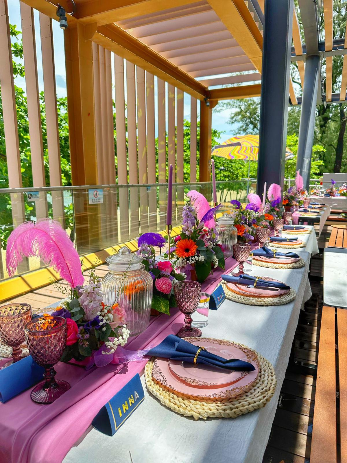Magenta and orange celebration tablescape — long table with florals, glassware and name cards styled beside the sea