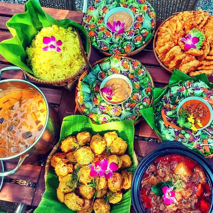 Overhead rainbow of Novy's Indonesian dishes — yellow rice, rice-paper rolls with orchids, curries, fritters and beef rendang on banana leaves