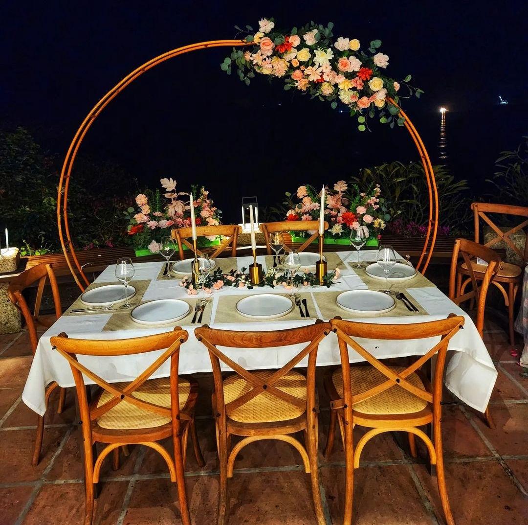 Private dinner table set at night with a floral hoop arch, gold candlesticks and white linen, overlooking the sea