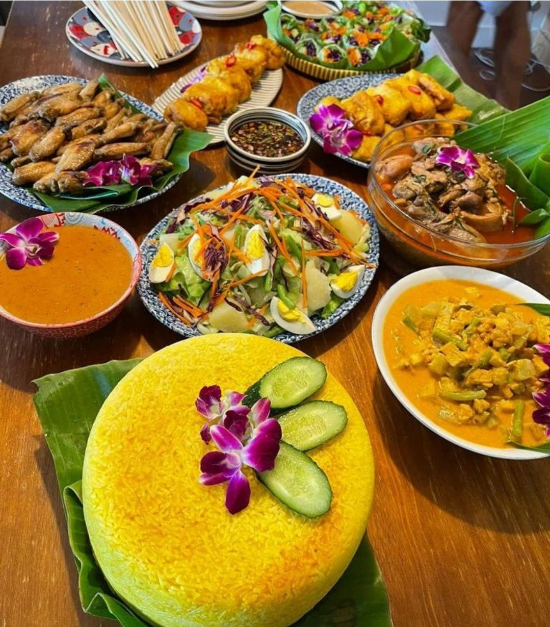 Nasi kuning wheel topped with orchids and cucumber surrounded by satay, curries, chicken wings and salad